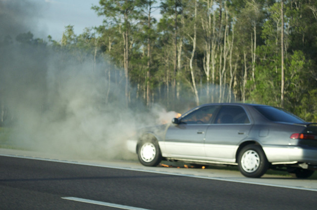 Car with engine fire and smoke on the side of the road, vehicle breakdown emergency