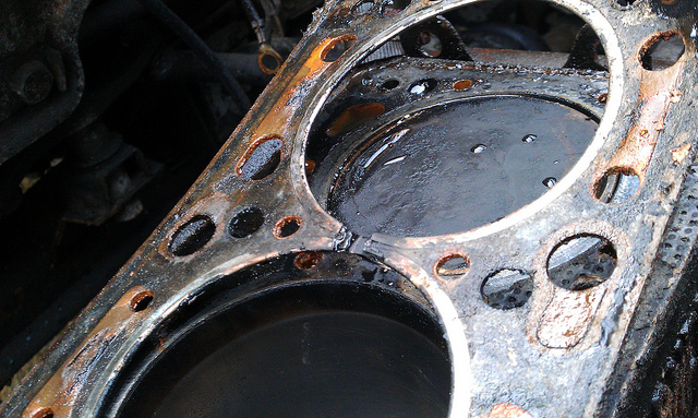 Close-up of a damaged car engine head gasket with visible wear and oil residue