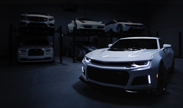 White Chevy Camaro in a dark garage with luxury cars on lifts in the background