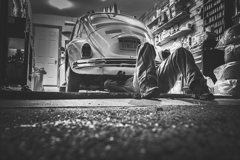 Mecánico trabajando debajo de un auto antiguo en un garaje, reparación de automóviles, mantenimiento de vehículos, autos clásicos