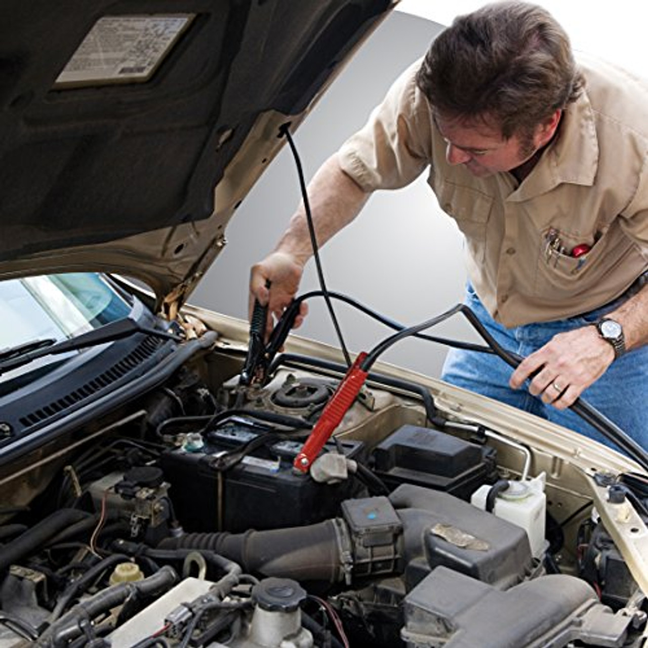 A man jump-starts a car battery using red and black jumper cables for emergency roadside assistance.